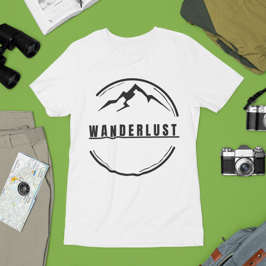 White t-shirt with 'Wanderlust' design on a green surface with travel-themed items.